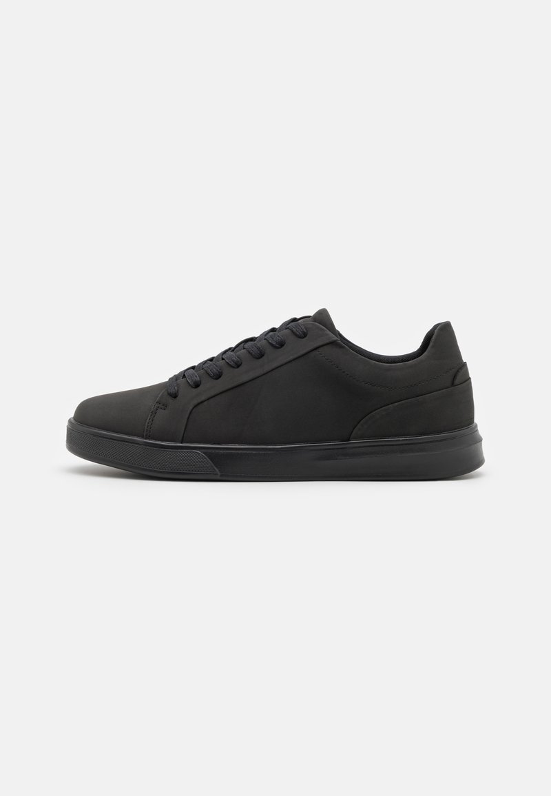 Chaussures de sport noires avec une texture lisse, un bout arrondi, une semelle intercalaire contrastante et des lacets noirs. Design minimaliste, adapté à un usage décontracté.