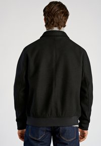 Svart fleecetröja med krage, synliga sömdetaljer, ribbade muddar och fåll. Bärs över denimjeans och visar upp ett strukturerat tyg.