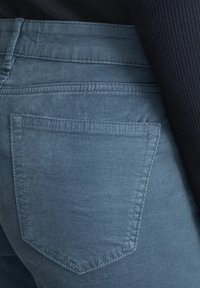 Modré denimové jeansy s hladkou textúrou, s zadnou vreckom oválneho tvaru a diskrétnou ševovou detailou.