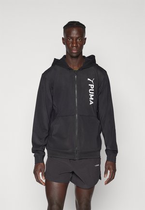 Black zip-up hoodie made of a smooth fabric, featuring a kangaroo pocket and white Puma logo on the left side. Worn with matching shorts.