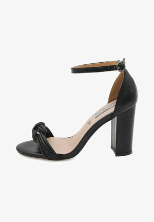 Sandalo nero con tacco alto, design anteriore annodato, punta aperta, cinturino alla caviglia regolabile e tacco spesso. Finitura in pelle liscia.