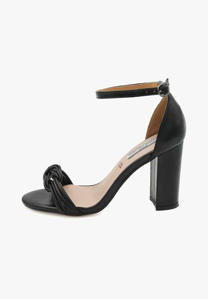 Sandalo nero con tacco alto, design anteriore annodato, punta aperta, cinturino alla caviglia regolabile e tacco spesso. Finitura in pelle liscia.