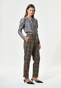 Bluse mit floralem Muster und Puffärmeln, kombiniert mit braunen Karottenhosen und schwarzen spitzen Schuhen mit einem tiefen Ausschnitt.
