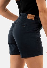 Pantalones cortos de algodón azul marino con un cinturón texturizado, que incluye una etiqueta de parche de cuero y un pequeño logo metálico en el bolsillo trasero.