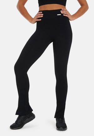 Black ribbed leggings with a high waistband and flared hems. Features a small metallic accent on the waistband. Made of stretchy material.