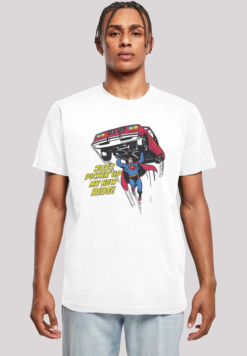 White cotton t-shirt featuring a comic-style graphic of a superhero lifting a red car, with yellow text reading, "JUST PICKIN' UP MY NEW RIDE!"