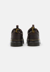 Brown leather sneakers with black rubber soles, yellow stitching, and back pull tabs for easy wear. Smooth texture and rounded shape.