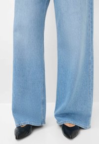 Jeans a gamba larga di colore blu chiaro con orlo sfrangiato, abbinati a tacchi neri a punta. Texture del denim visibile; il design elegante delle scarpe accentua la forma delle gambe.