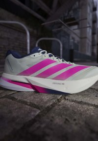 Chaussure de running Adidas blanche et rose sur le trottoir avec "Lightstrike Pro" visible sur la semelle intermédiaire et le textile supérieur en mesh.