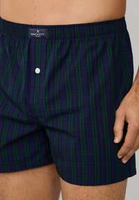 Kraťasy v tmavě zelené a námořnické kostce, s elastickým pasem a předním knoflíkovým zapínáním, vyrobené z lehkého materiálu.