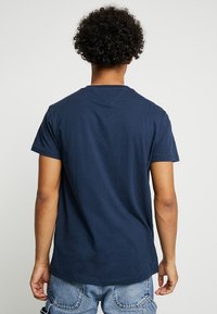 Námořnická modrá bavlněná tričko s krátkými rukávy, kulatým výstřihem a rovnými liniemi. Zadní strana je jednoduchá, bez viditelných log nebo vzorů.