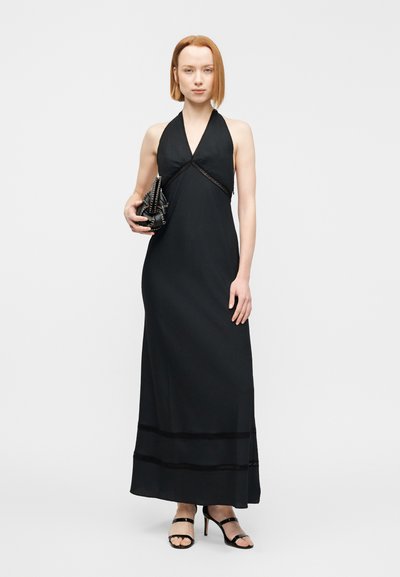 Μαύρο φόρεμα μάξι με χιαστί λαιμόκοψη, δαντελένιες λεπτομέρειες, απαλό ύφασμα και ελαφρώς φαρδύ τελείωμα. Συνδυασμένο με μαύρο τσαντάκι με υφή και ψηλοτάκουνα πέδιλα με λουράκια.