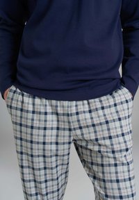 Persona che indossa una maglietta a maniche lunghe blu e pantaloni a quadri bianchi con linee navy e rosse, con le mani infilate nelle tasche dei pantaloni.
