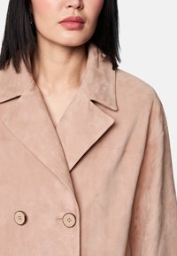 Doppelt geknöpfter Mantel aus rosa Wildleder mit großen, runden beigen Knöpfen und einem Reverskragen, mit einer strukturierten, glatten Oberfläche.