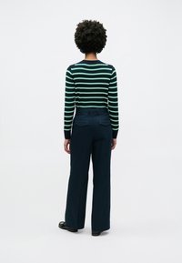 Πλεκτό πουλόβερ με ρίγες σε ναυτικό μπλε, πράσινο και άσπρο, συνδυασμένο με παντελόνι παντελόνα σε ναυτικό μπλε με δύο πίσω τσέπες.