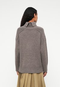 Hnedý pletený sveter s vysokým golierom, raglánovými rukávmi a rebrovaným lemom. Textil má jemnú štruktúru s jemným melírovaným vzorom.