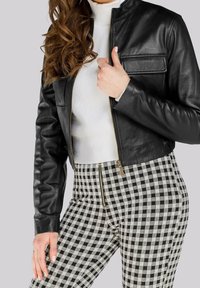 Black leather cropped jacket with a stand collar and a zippered front, paired with black-and-white checked high-waisted pants with zippers.
