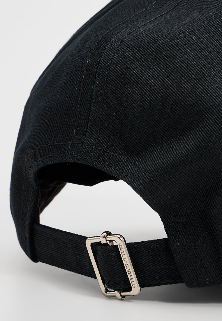 Gorra de algodón negra con tela texturizada y una correa ajustable con un hebilla de metal plateada. Detalle del logo en la hebilla.