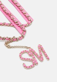 Chaîne en or avec du cuir rose tissé, arrangée pour épeler "SM" sur un fond blanc.