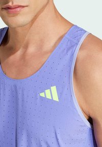 Camiseta sin mangas de tela púrpura clara con pequeñas perforaciones, que presenta un logo verde lima y bordes lisos.