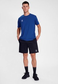 Camiseta azul de manga corta con un logo, combinada con pantalones cortos deportivos negros. Calcetines negros y zapatillas de running completan el conjunto. Diseño sencillo y deportivo.