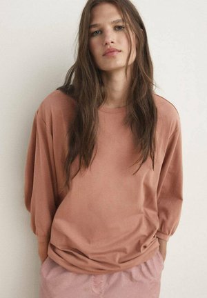 Ljusrosa oversized sweatshirt med långa, lösa ärmar och rund nacke, i kombination med ljusrosa byxor. Slät tygtextur.