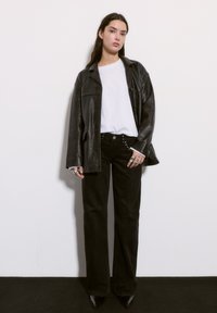 Čierna kožená bunda cez biele tričko, doplnená vysokými čiernymi džínsami so zdobnými gombíkmi a špicatými čiernymi lodičkami.