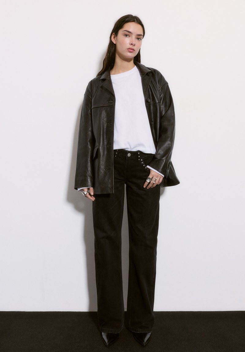 Čierna kožená bunda cez biele tričko, doplnená vysokými čiernymi džínsami so zdobnými gombíkmi a špicatými čiernymi lodičkami.