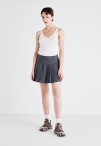 Fustă plisată gri cu un talie ajustată, asortată cu un maiou alb și adidași maro. Design minimalist, textură ușoară a materialului.