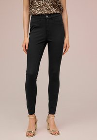 Jeans negros ajustados con una textura suave y un diseño clásico de cinco bolsillos, combinados con unos tacones dorados con tiras. La parte superior presenta un patrón de estampado de leopardo.