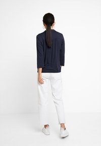 Navy-blaues Polka-Dot-Oberteil mit Dreiviertelärmeln, strukturiertem Stoff, kombiniert mit weißen weiten Hosen und weißen Turnschuhen. Schlichtes Design, lässige Passform.
