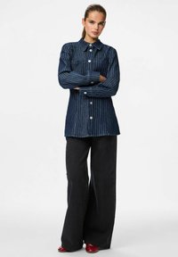 Camisa de mezclilla de mangas largas con rayas blancas verticales, cuello con solapa y botones frontales, combinada con pantalones de tiro alto de pierna ancha negros.