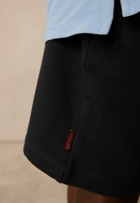 Svarta bomullsshorts med rak skärning, med en röd "SUPERDRY"-etikett på den nedre sidan och en slät textur.
