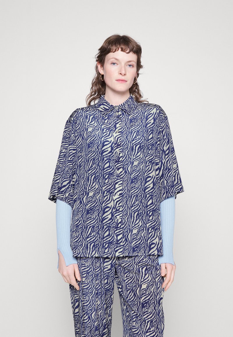 Kurzärmlige Bluse mit einem auffälligen Marineblau und weißen Wirbelmuster, mit Kragen-Design, kombiniert mit passenden Hosen und hellblauen gerippten Ärmeln.
