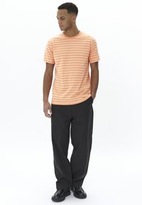 Striped orange T-shirt with short sleeves, round neckline, paired with black, loose-fitting pants and black shoes.