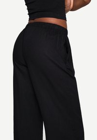 Black wide-leg trousers with an elastic waistband, featuring a breathable texture and side pockets, shown from a side angle.