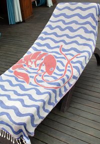 Lounge chair on wooden deck covered with towel featuring blue wavy stripes and a large red lobster design.