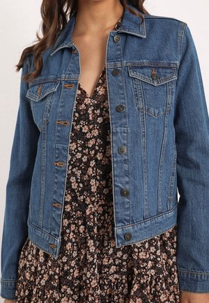 Kvinde iført en blå denimjakke over en sort kjole med blomsterprint, V-hals og lange ærmer.