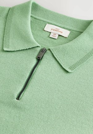 Pull en maille vert à col montant avec fermeture par demi-zip et tissu texturé. Étiquette indiquant "NEXT SIGNATURE," taille M.