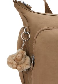 Borsa in tela color sabbia con tasca con zip, dotata di un charm a forma di scimmia beige soffice attaccato da una catena e anello portachiavi in argento. Tessuto dal design testurizzato.