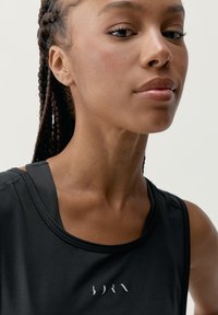 Czarny sportowy top bez rękawów o minimalistycznym wzornictwie, z okrągłym dekoltem i logo nadrukowanym z przodu. Gładka tekstura materiału.