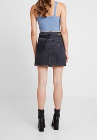 Gonna mini in denim nero con orlo sfilacciato, due tasche posteriori e branding sulla vita, abbinata a una canotta a righe blu chiaro e stivaletti neri alla caviglia.