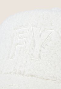 Cappello bianco texturizzato con un logo ricamato "FY" in un colore avorio. Il materiale appare soffice e peloso, con una forma arrotondata.
