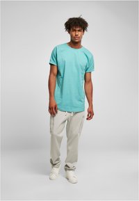 Camiseta de algodón color turquesa con mangas enrolladas, combinada con pantalones de chándal ligeros grises con bolsillos, usados con zapatillas blancas.