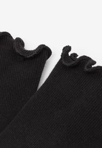Calze nere a coste con bordo arricciato. La texture è liscia con una leggera lucentezza; le arricciature aggiungono un dettaglio decorativo nella parte superiore.