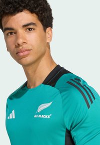 Tealfärgad sporttröja med svarta accenter, med rundad halsringning, tre-randig design på axlarna och "All Blacks"-logotyp på bröstet.