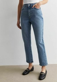 Pantalones tejanos de cintura alta en azul, hechos de mezclilla, con un corte recto, que cuentan con un diseño clásico de cinco bolsillos y sutiles desgastes. Mocasines negros con detalles dorados.