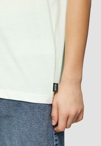 Lichtgroene katoenen t-shirt met korte mouwen, voorzien van een zijlabel in donker groen met de tekst "SLVR." Draagt met blauwe spijkerbroeken.