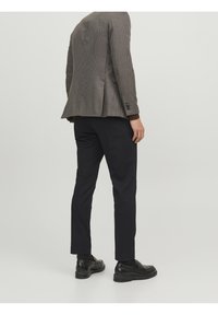 Brązowa marynarka w kratę o dopasowanym kroju, zestawiona z ciemnymi spodniami typu slim fit i czarnymi skórzanymi butami. Charakteryzuje się fakturowanym materiałem i eleganckim designem.