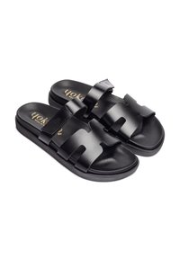 Sandales noires avec un dessus en synthétique lisse, deux larges sangles et une semelle intérieure moulée, montées sur une semelle plate. Détail du logo doré visible.